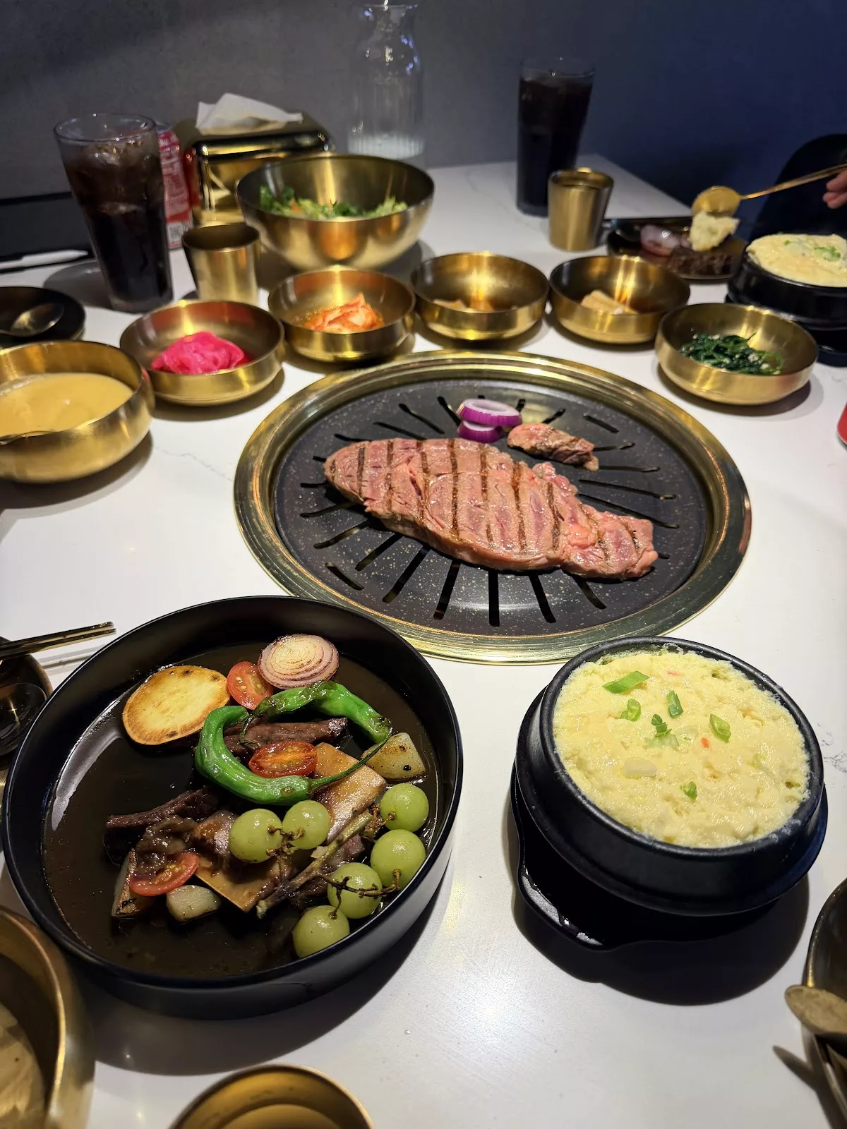 Steak sizzling at an Inju table, surrounded by banchan, braised short ribs and corn cheese